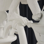Close view of a monkey's hand and arm gripping a curved arm of this white Clérachic chandelier, with the textured resin visible.
