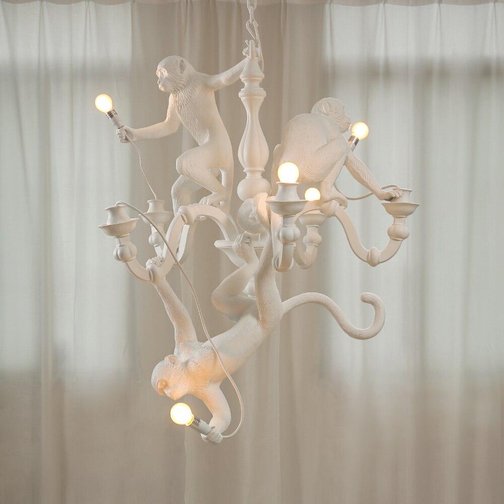 White Clérachic monkey chandelier lit in front of sheer curtains, with warm light on the monkeys and curving arms.