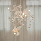 White Clérachic monkey chandelier lit in front of sheer curtains, with warm light on the monkeys and curving arms.