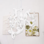 White Clérachic monkey chandelier beside a framed leaf print on a pale wall, one monkey hanging low by the arms.