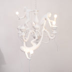 Lit white Clérachic monkey chandelier hung in front of a pale wall, with one monkey hanging below holding a glowing bulb.
