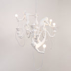 White Clérachic chandelier with the monkeys' bulbs lit, hung in front of a plain pale wall and trailing a white cable.
