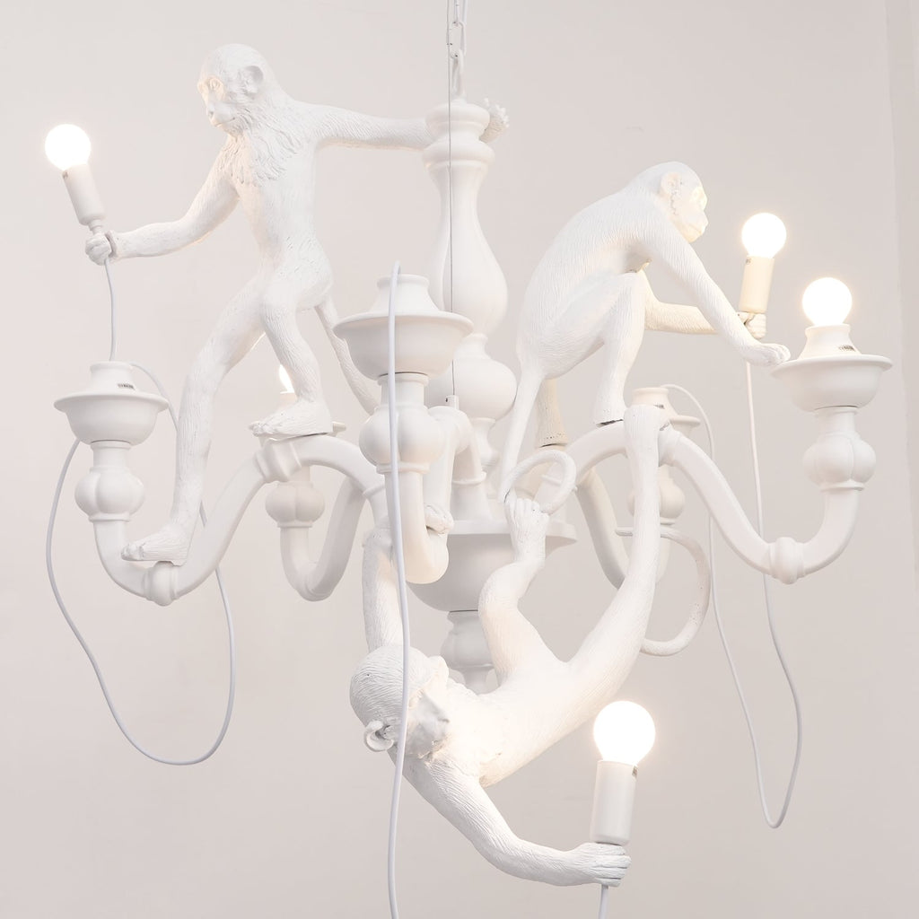 Close view of the monkeys and bowl-shaped candle cups on this white Clérachic chandelier, with a bulb in the lowest monkey's hand.