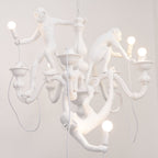 Close view of the monkeys and bowl-shaped candle cups on this white Clérachic chandelier, with a bulb in the lowest monkey's hand.