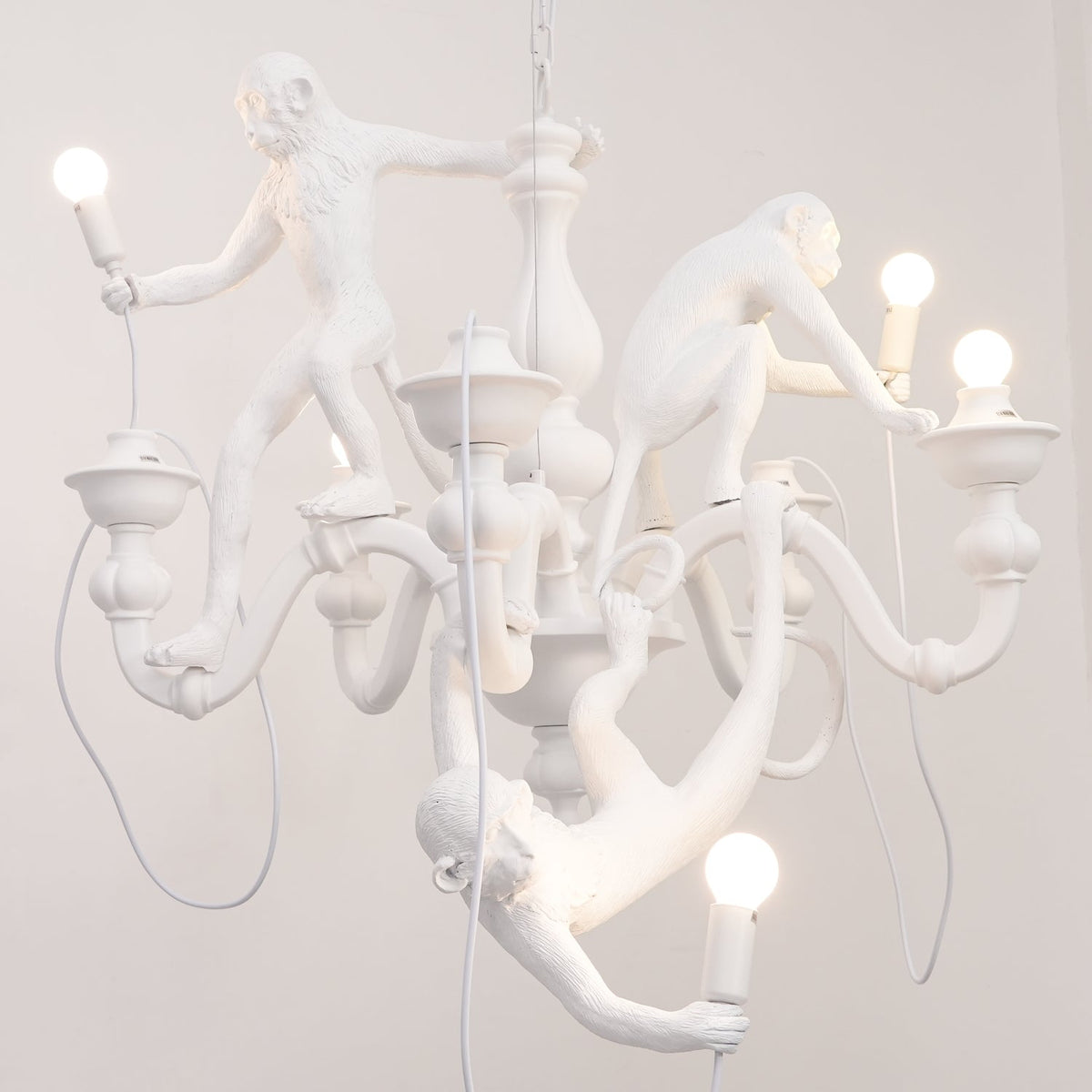 Close view of the monkeys and bowl-shaped candle cups on this white Clérachic chandelier, with a bulb in the lowest monkey's hand.