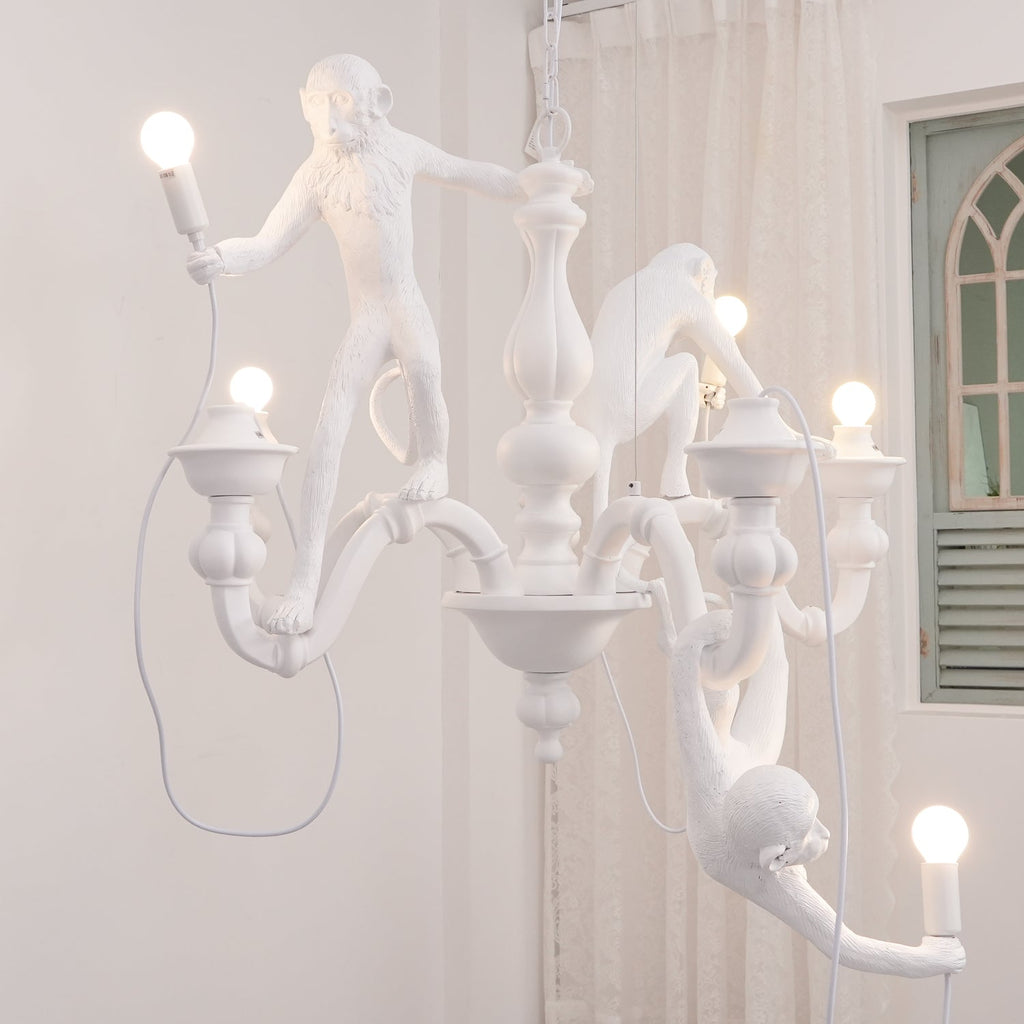 White Clérachic chandelier lit in a room with a sheer curtain and a green arched window, one monkey stretching toward a bulb.