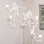 White Clérachic chandelier lit in a room with a sheer curtain and a green arched window, one monkey stretching toward a bulb.
