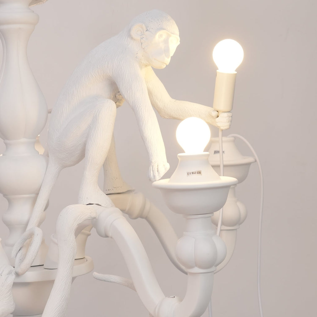 Close view of a resin monkey sitting on the stem and holding a bulb, beside a lit candle cup on this Clérachic chandelier.