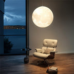 Clérachic moon pendant glowing softly over a cream leather lounge chair and a lake view at dusk.