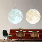 Clérachic two crater-textured moon pendants, one lit cool white and one warm white, above an orange banquette and dining chairs.