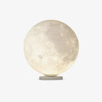 Clérachic moon table lamp, a white sphere with a cratered surface glowing warm on a slim round base, on a plain light backdrop.