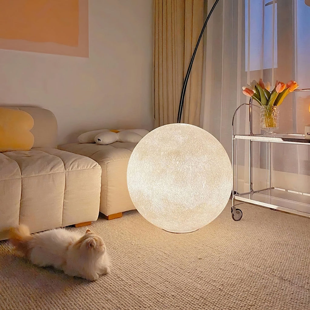 Clérachic moon sphere lit in a cosy living room, with a cat on the carpet, a tufted sofa and a trolley of tulips behind.