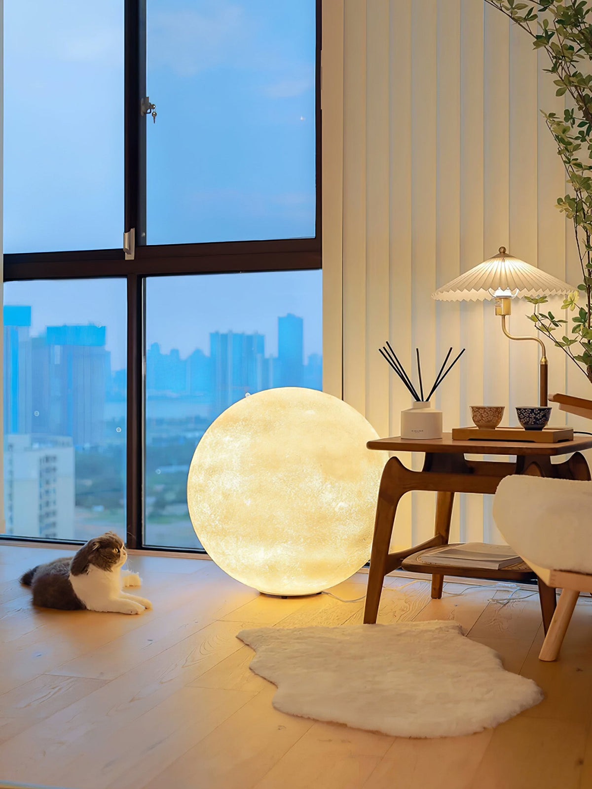 Seen from further back, this Clérachic moon lamp glows low in a bright corner with a tall window, a cat and a fur rug.