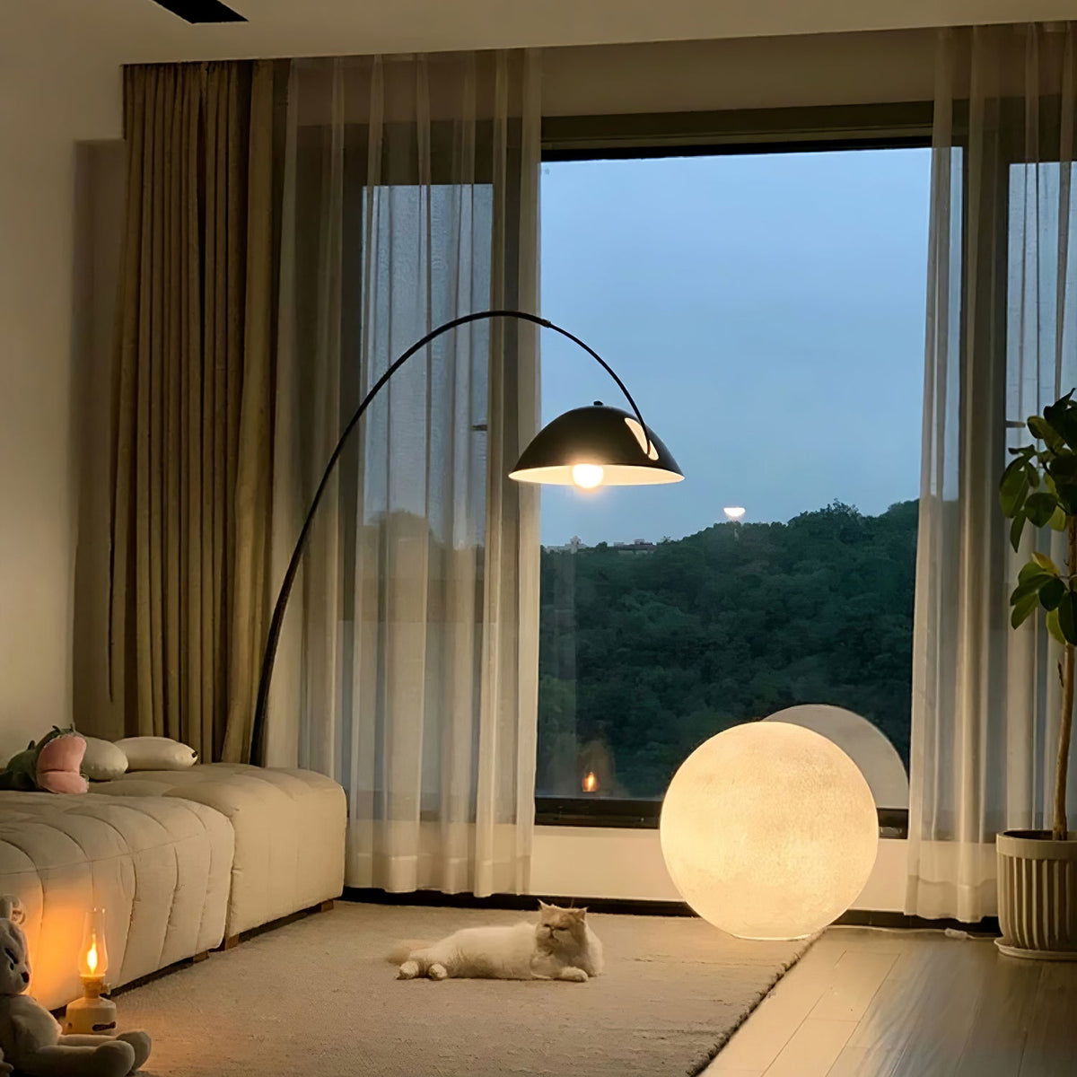 A Clérachic moon lamp glows by a large window with a hill view, below an arched floor lamp and near a cream modular sofa.