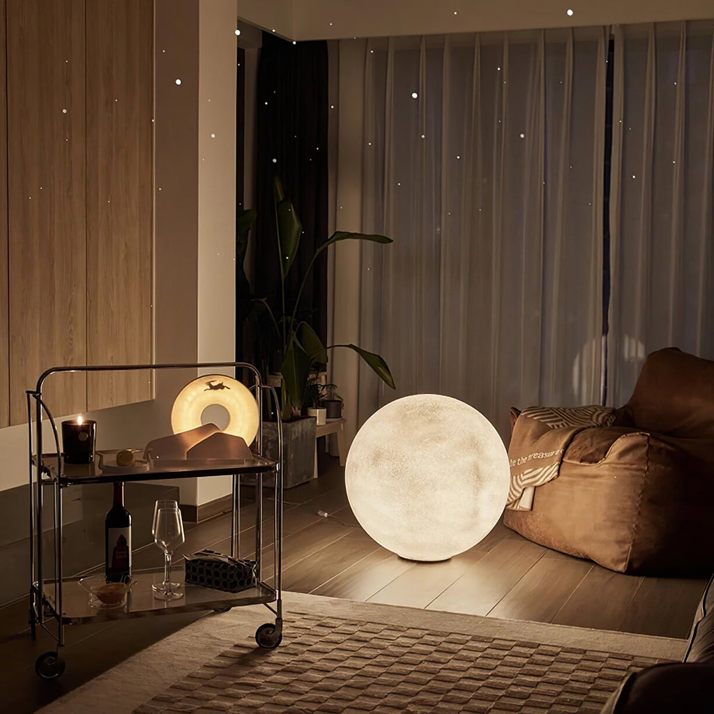 Evening view of this Clérachic moon lamp by a dark metal trolley with a candle and a glass, with a beanbag chair beside it.