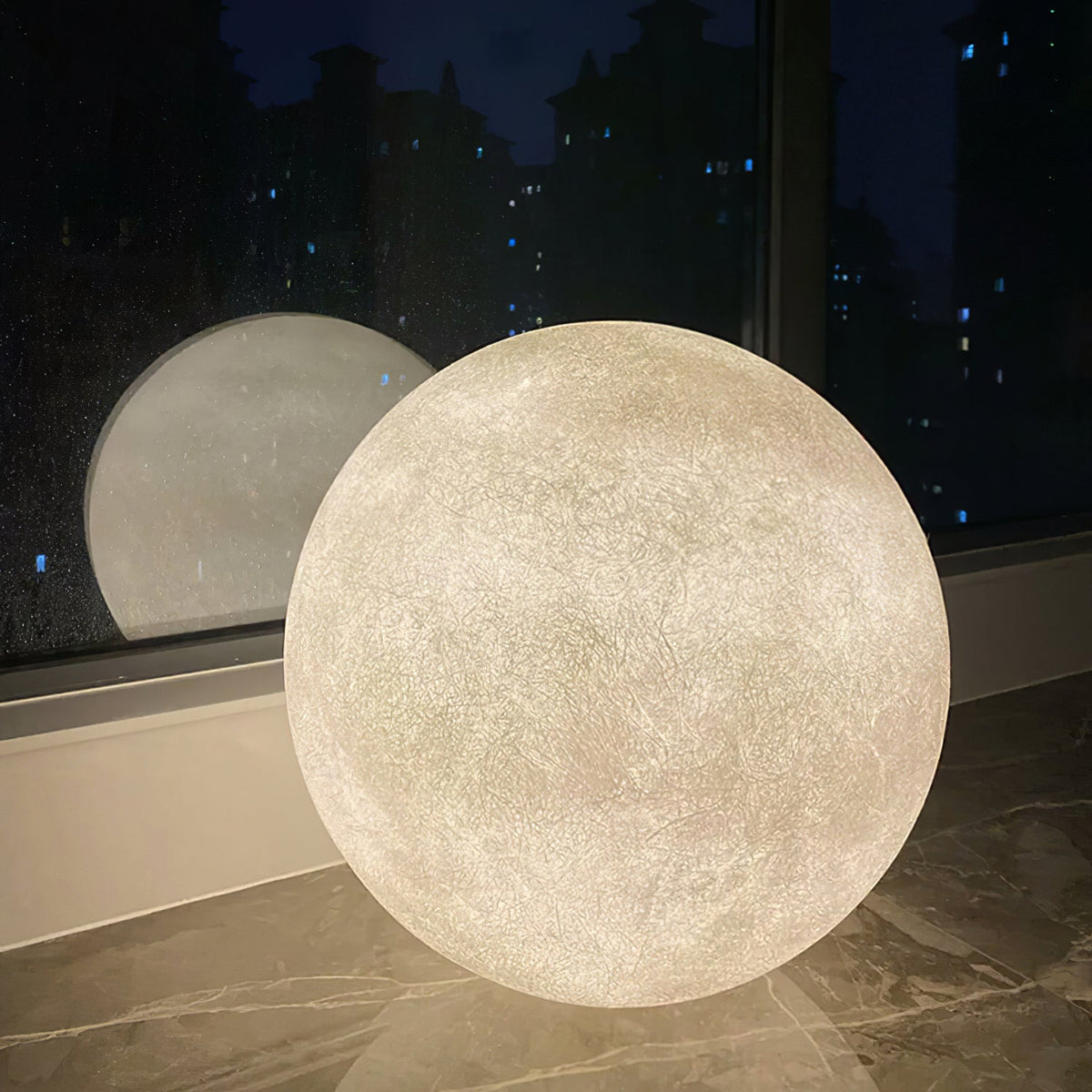 Close view of a big Clérachic moon sphere glowing on a dark stone floor in front of a night window, with a reflection behind.