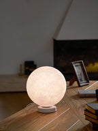 This Clérachic moon table lamp glows pink-white on a round white base, standing on a wooden desk with a photo frame and books.