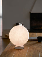 A closer view of the lit Clérachic moon table lamp on a wooden desk, its cratered surface glowing warm against a blurred dark wall.