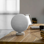 Angled view of the unlit Clérachic moon table lamp on a wooden desk, with a photo frame and books behind it.
