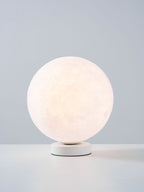 A smaller view of the lit Clérachic moon table lamp, glowing soft white on its base against a blue-grey backdrop.