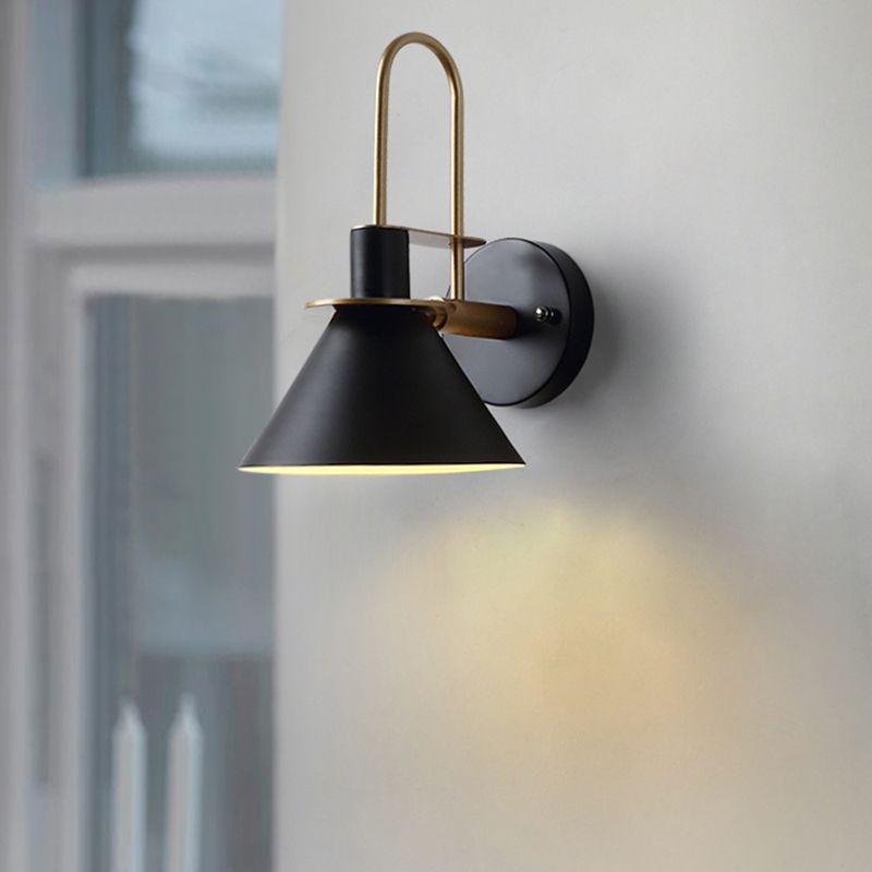 Clérachic Morandi horn-shade wall sconce in black, its brass arch catching daylight as it washes warm light down a pale wall.