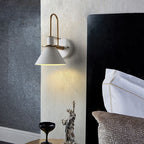 The white Clérachic Morandi horn-shade wall sconce mounted beside a black headboard, throwing a soft cone of light down the bedside wall.
