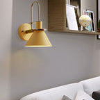 Clérachic Morandi horn-shade wall sconce in mustard yellow above a living-room sofa, its brass carry-handle arch arcing over the cone.