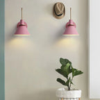 Two pink Clérachic Morandi horn-shade wall sconces spaced along an entryway wall, each pooling warm light beside a straw hat and a plant.