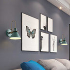 Green Clérachic Morandi horn-shade wall sconces bracketing a gallery wall of framed prints above a bed, lighting the pictures from each side.