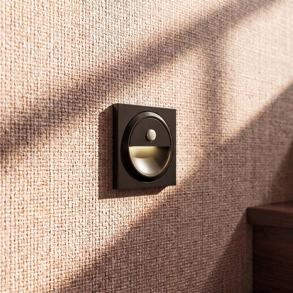 Clérachic black square wall light with a glowing half-moon recess on a woven grasscloth wall by a staircase.