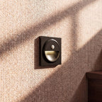 Clérachic black square wall light with a glowing half-moon recess on a woven grasscloth wall by a staircase.