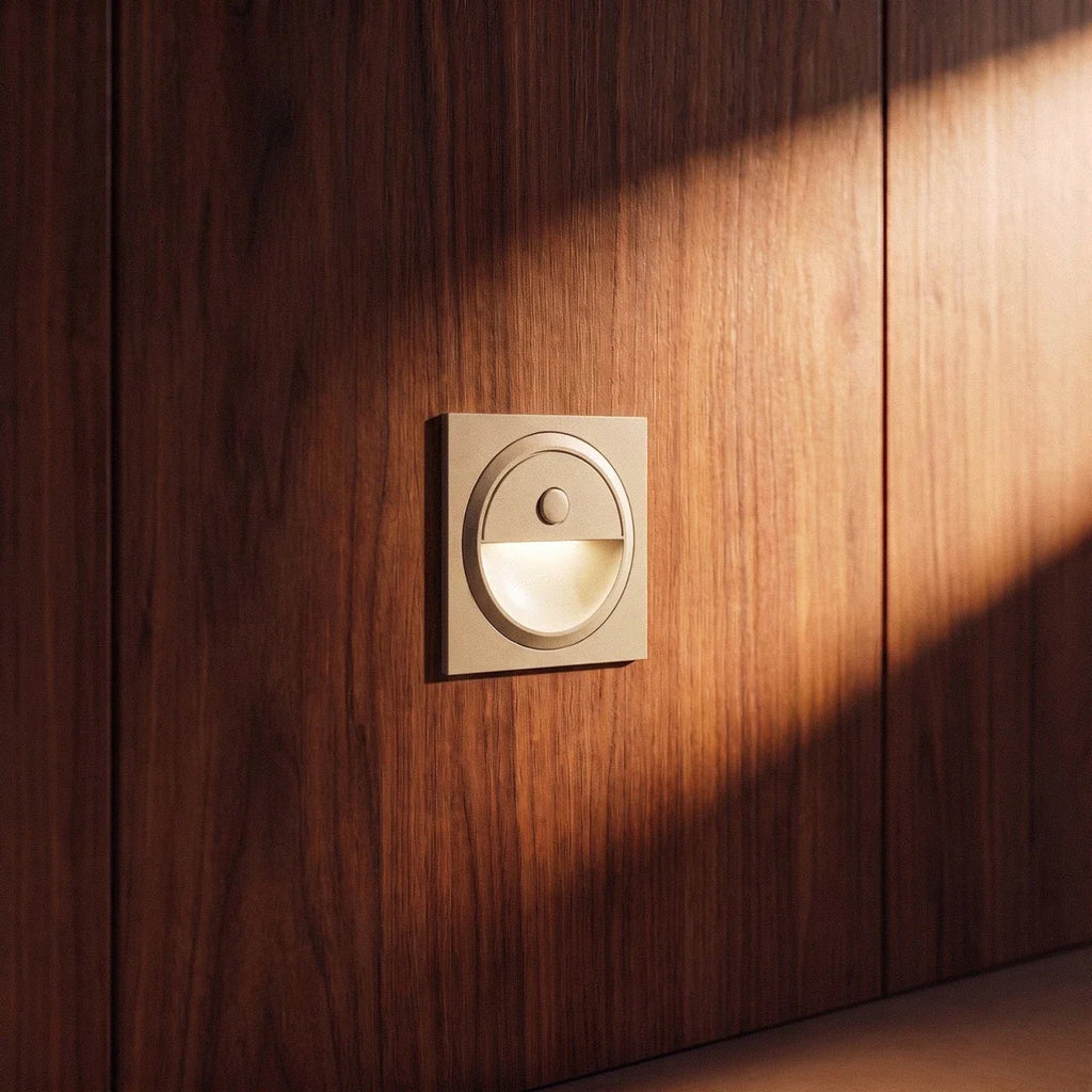 Clérachic pale square wall light glowing warm on a walnut-veneer wall, with sunlight sweeping across the panel.