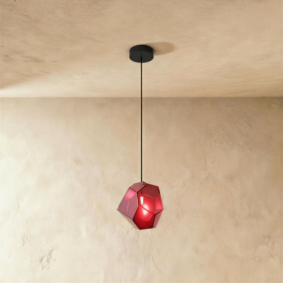 A Clérachic faceted glass pendant in deep rose red hangs on a black cord against a warm plastered ceiling corner.