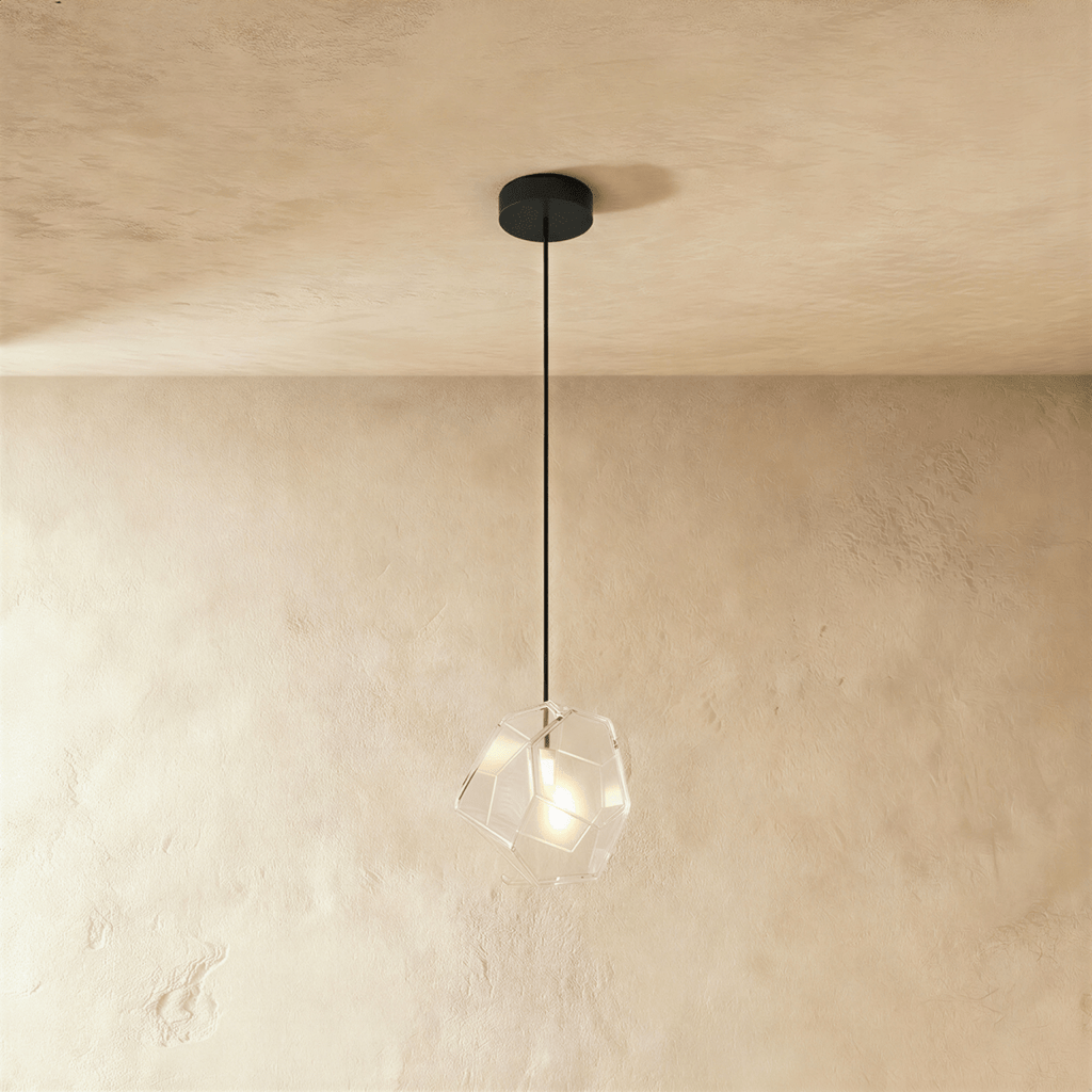 A Clérachic faceted glass pendant in clear glass hangs on a black cord against a warm plastered ceiling corner.