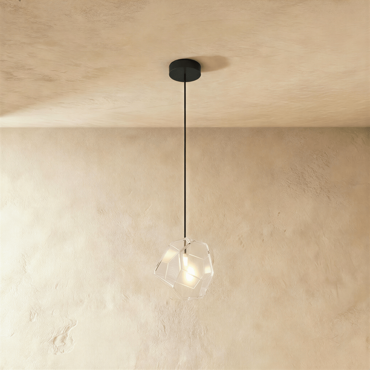 A Clérachic faceted glass pendant in clear glass hangs on a black cord against a warm plastered ceiling corner.