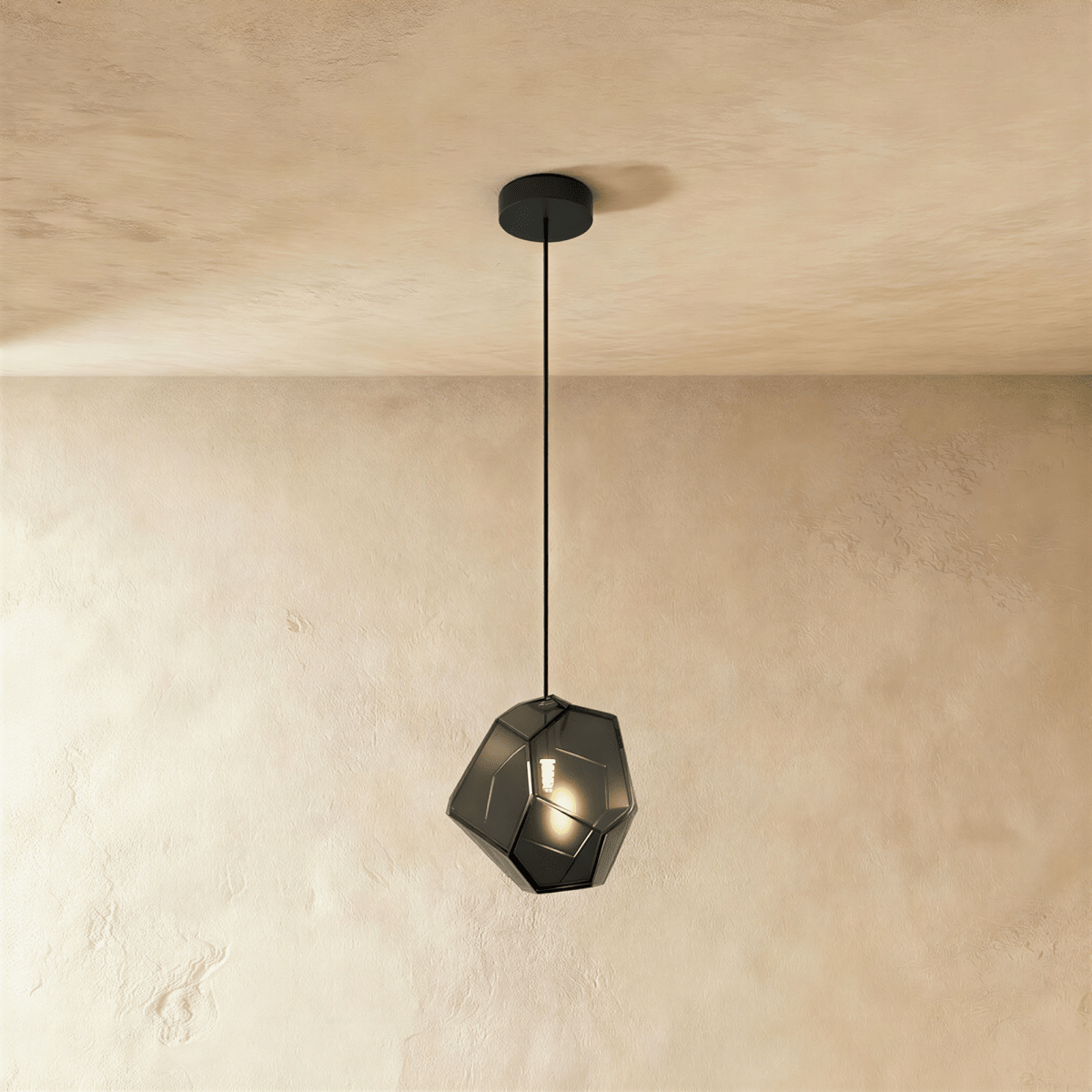 A Clérachic faceted glass pendant in smoked light gray hangs on a black cord against a plastered ceiling corner.