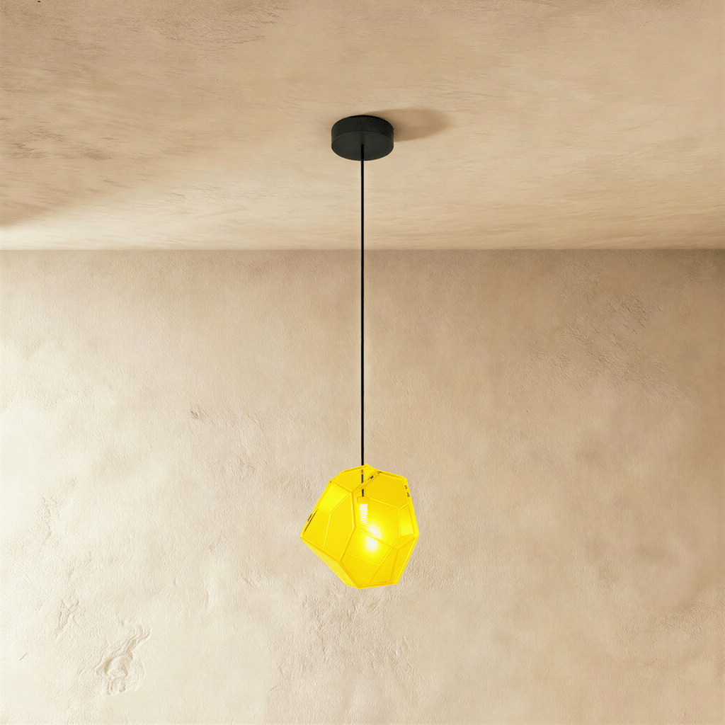 A Clérachic faceted glass pendant in bright yellow hangs on a black cord against a warm plastered ceiling corner.