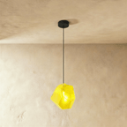 This Clérachic pendant's yellow faceted glass glows brightly, the bulb visible through its angled cut panes.