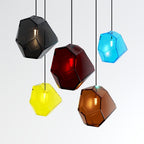 Five Clérachic faceted glass pendants in gray, rose red, yellow, brown and blue hang together on a plain backdrop.