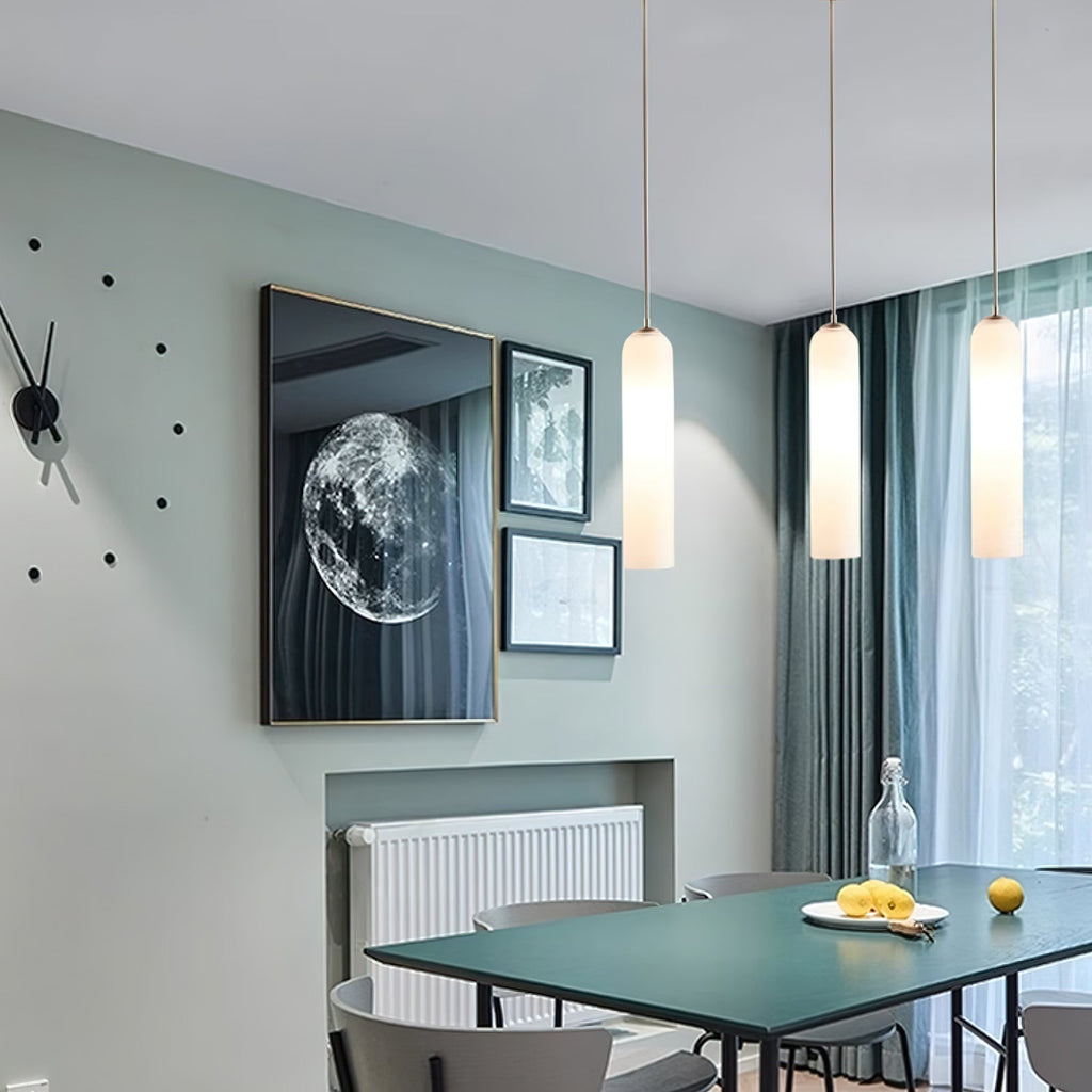 Three frosted white Clérachic pendants lit above a dining table, with a round mirror and framed art on a sage wall.