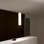 A frosted white Clérachic tube pendant lit in a dark corner, above a counter styled with small ceramic cups.