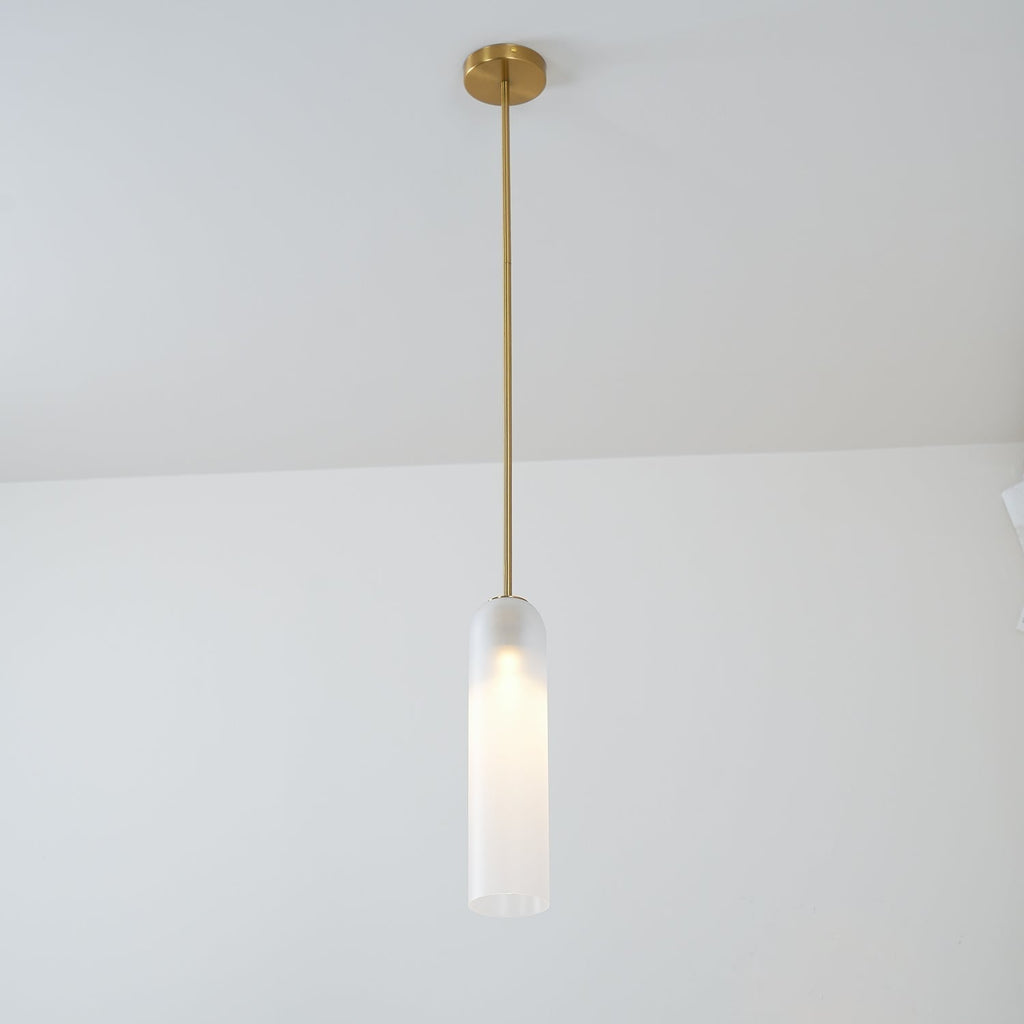 A frosted white Clérachic tube pendant lit on a brass rod, hung in a bright room with a sheer curtain at the edge.