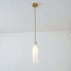 A frosted white Clérachic tube pendant lit on a brass rod, hung in a bright room with a sheer curtain at the edge.