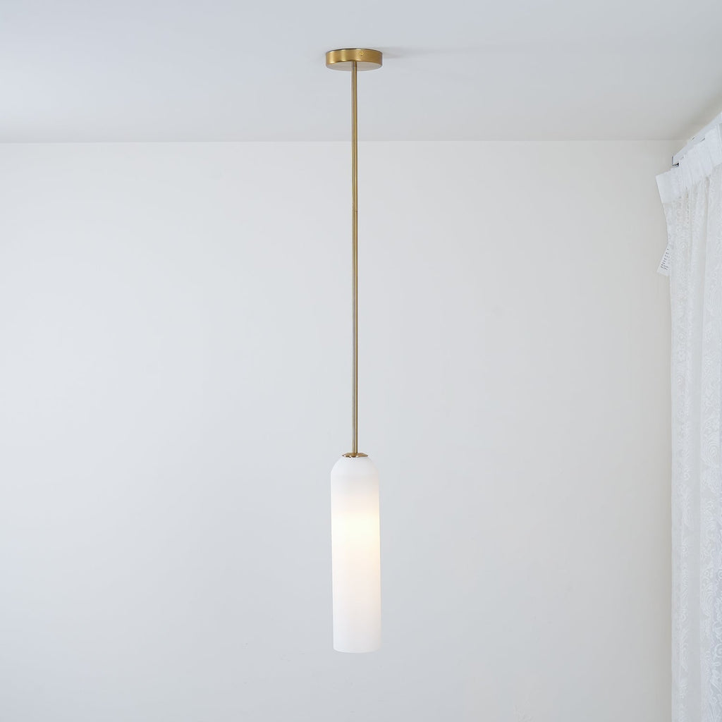 The frosted white Clérachic pendant lit on a brass rod, its glass catching light near a curtained window corner.
