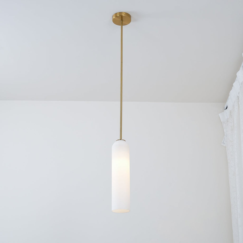 A frosted white Clérachic tube pendant lit on a brass rod, hung close to a lace curtain in a sunlit room.
