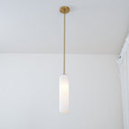 A frosted white Clérachic tube pendant lit on a brass rod, hung close to a lace curtain in a sunlit room.