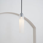The frosted white Clérachic pendant on a black rod, lit, its glow warming the curve of a rounded archway below.