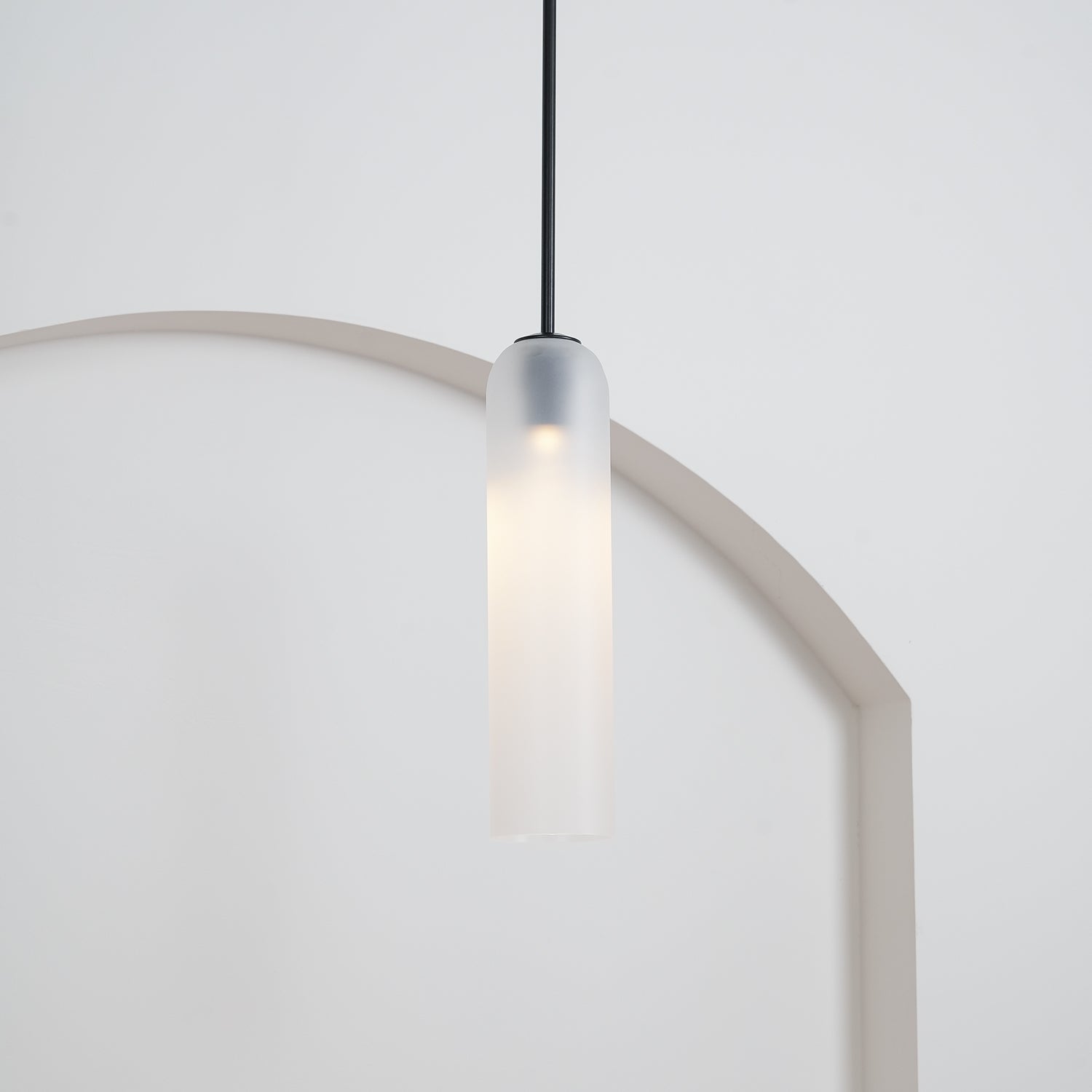 The frosted white Clérachic pendant on a black rod, lit, its glow warming the curve of a rounded archway below.