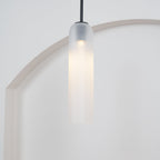 The frosted white Clérachic pendant on a black rod, lit, centred in front of a circular cut-out wall opening.