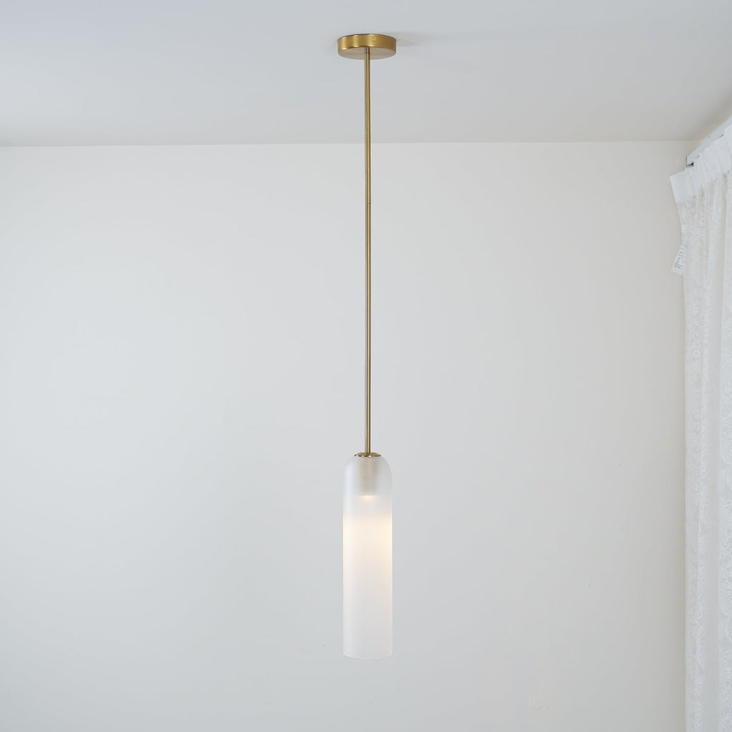 The frosted white Clérachic pendant on a brass rod, lit, its long stem reaching down near a curtained window.